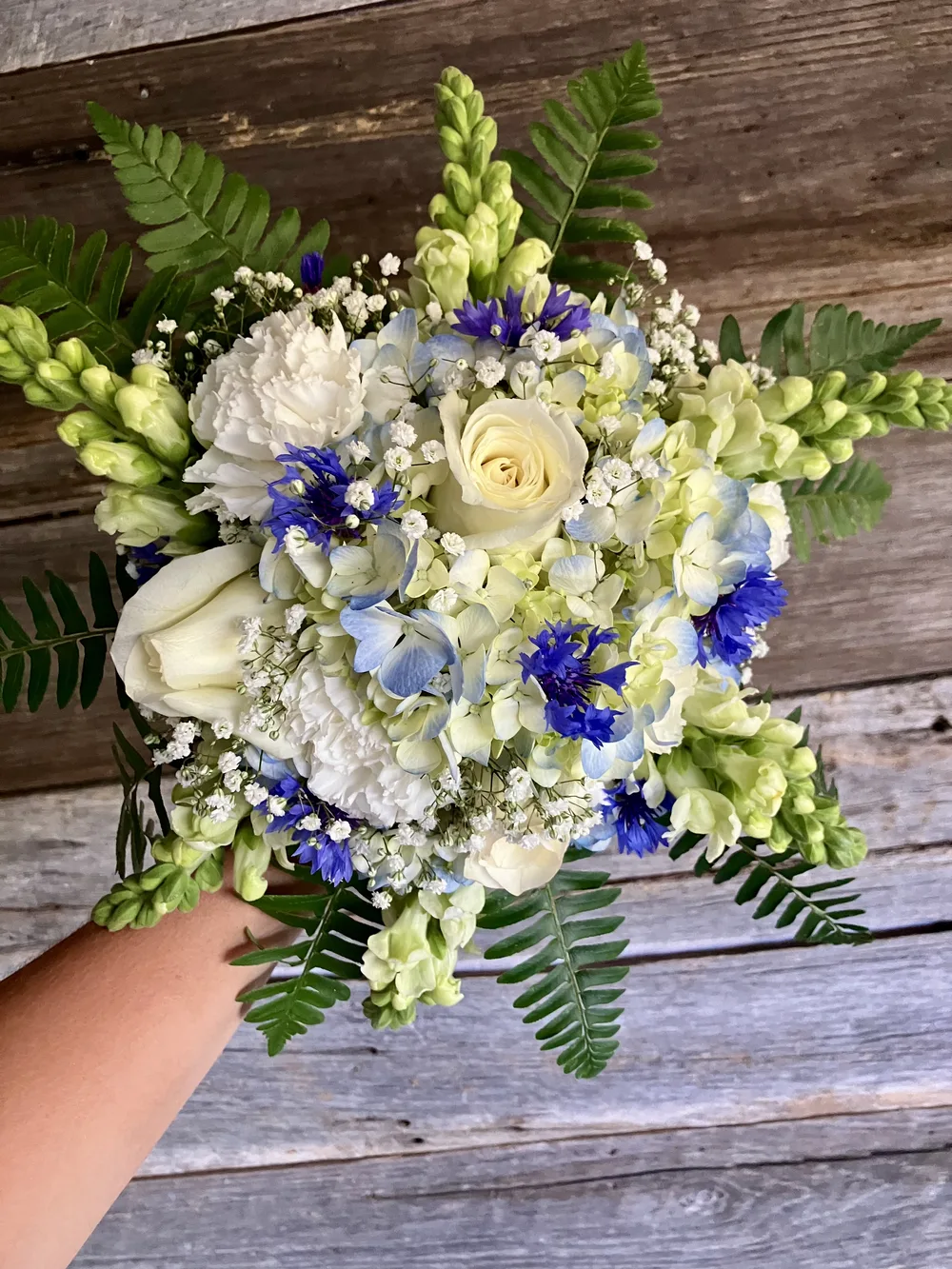 Hand-tied bouquet of blue hydrangeas, white roses, and greenery