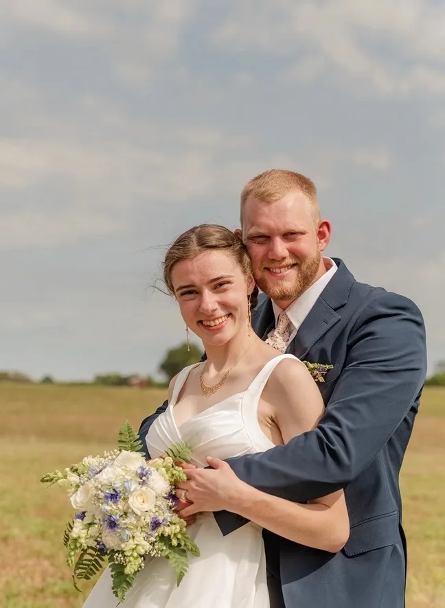Newlywed couple holding a blue, white, and greenery bouquet
