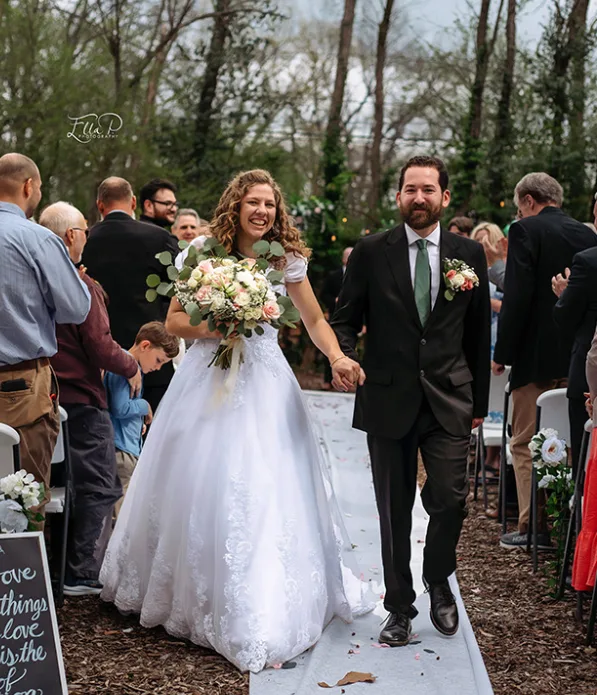 Newlyweds walking down the aisle with a soft pink and white bouquet